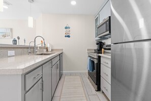 Une cuisine moderne dotée d’appareils électroménagers en acier inoxydable, d’un plan de travail en granit et d’un petit tapis.