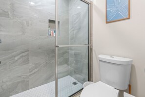 Une salle de bain avec une douche à parois de verre, des toilettes et une œuvre d’art représentant une étoile de mer au mur.