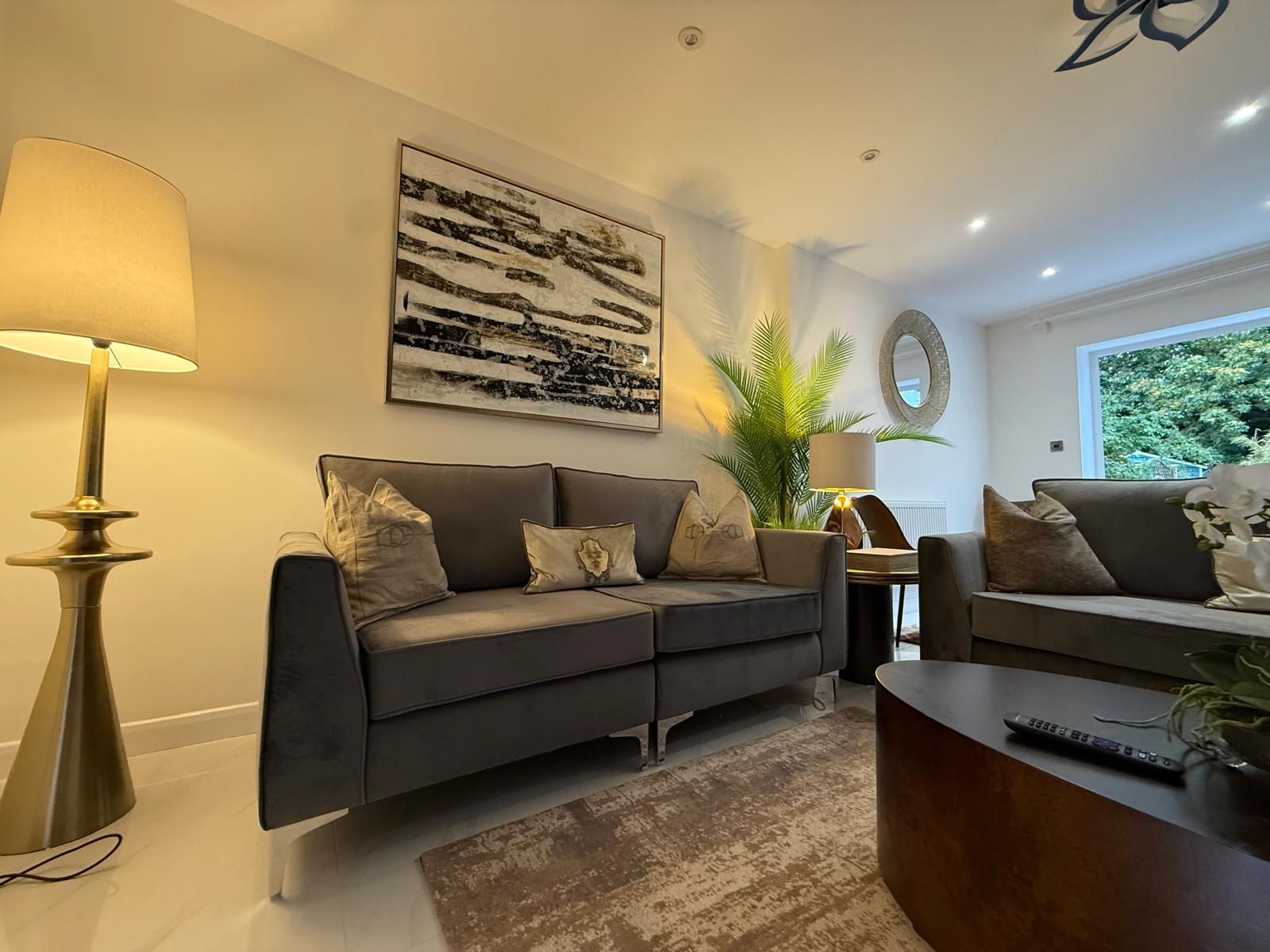 A modern living room with a grey sofa, a coffee table, a lamp, and a painting on the wall.