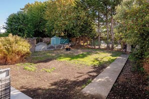 Ein Garten mit einem gepflasterten Weg, einem kleinen Schuppen und verschiedenen Bäumen und Sträuchern.