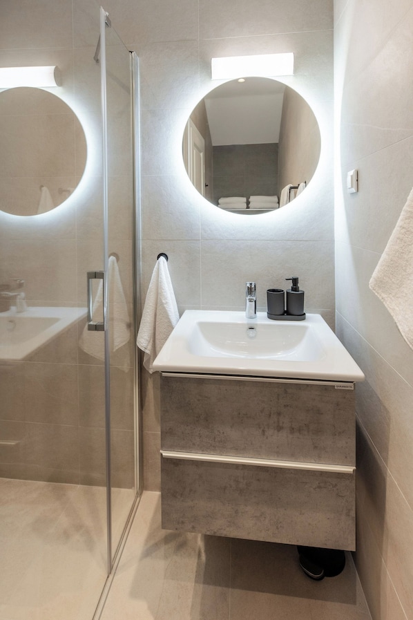 Une salle de bain moderne avec une douche à parois de verre, un lavabo blanc avec un miroir au-dessus et un porte-serviettes.