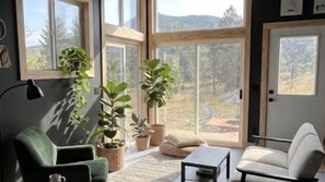 Un salon moderne avec de grandes fenêtres, un fauteuil vert, un canapé blanc et des plantes en pot.