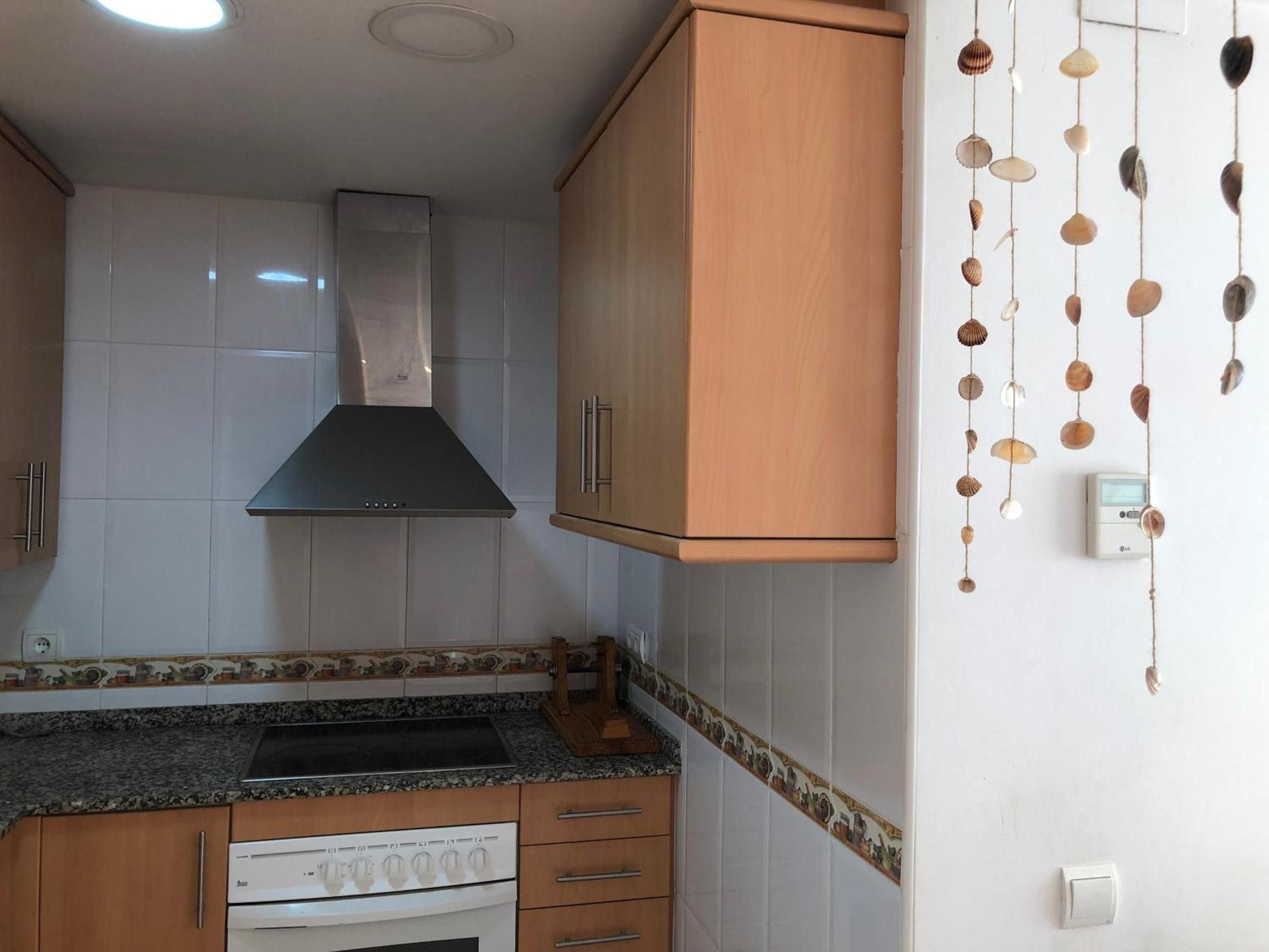 Een keuken met witte kasten, een roestvrijstalen afzuigkap, een granieten aanrechtblad en een fornuis.