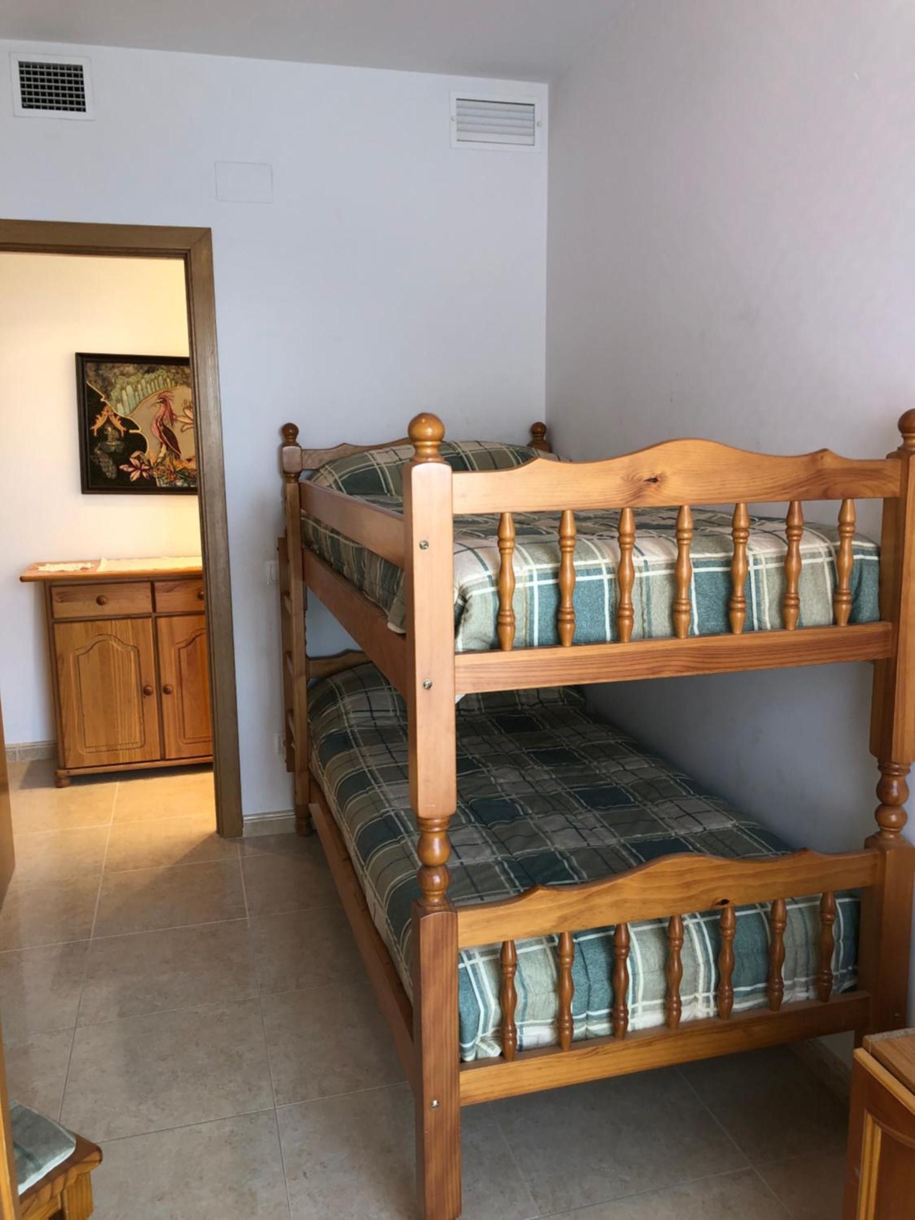 Un lit superposé avec une structure en bois et une literie à carreaux, une armoire en bois et un tableau accroché au mur.