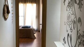Un couloir menant à une chambre à coucher, où se trouvent un lit, une décoration suspendue et un mur orné d’un motif décoratif.