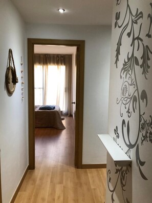 Een gang die leidt naar een slaapkamer met een bed, een hangende decoratie en een muur met een decoratief patroon.