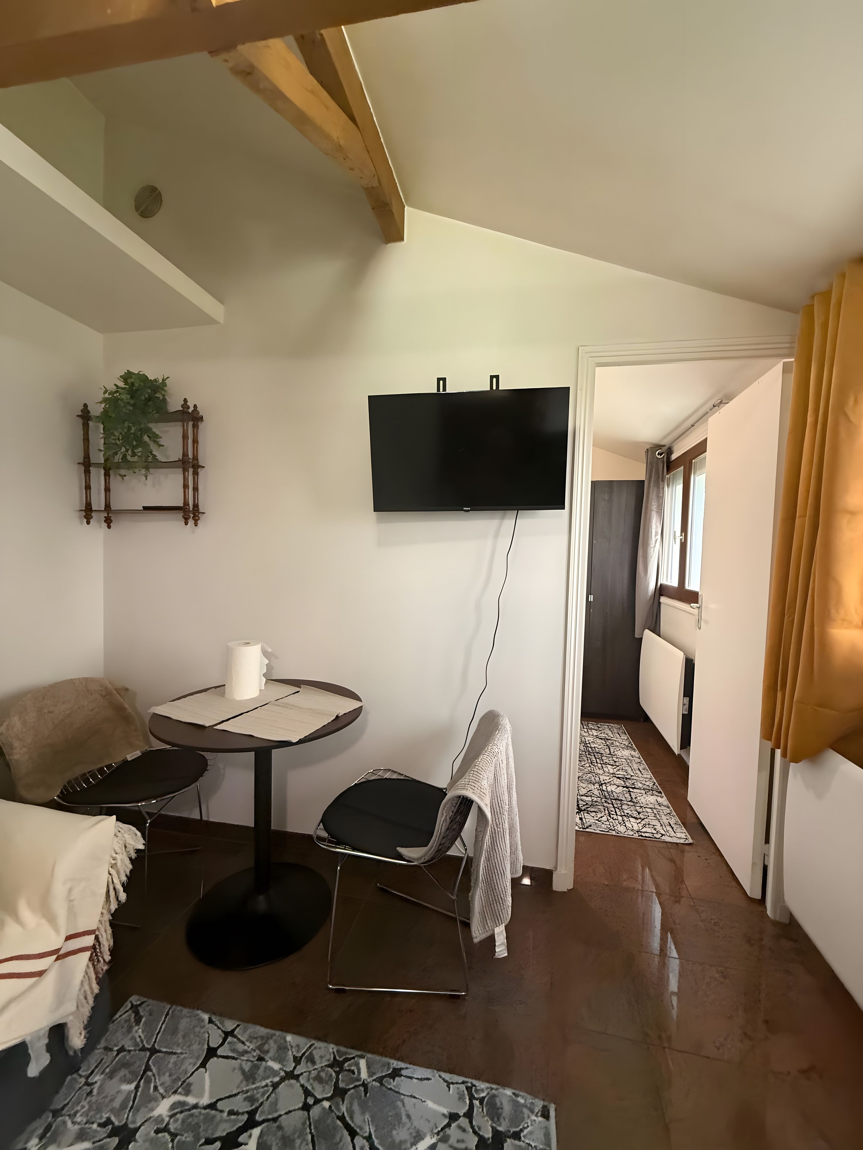 Un espacio habitable compacto con un televisor de pantalla plana montado en la pared, una pequeña mesa redonda con una silla, un sofá y una alfombra estampada.