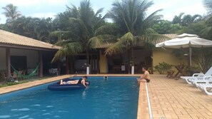 Piscina com área de estar, palmeiras e telhado cerâmico.