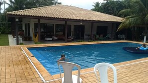 Piscina com área de varanda coberta, uma espreguiçadeira e uma rede.