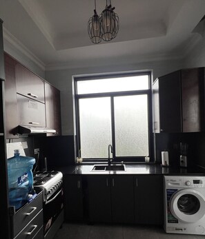 A kitchen with a large window, a stove, a sink, cabinets, and a washing machine. - CosyNook apartments (Kigali)