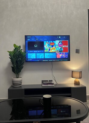 Televisor de pantalla plana fixat a la paret, que mostra una interfície multimèdia amb opcions com 'HOME', 'APPS', 'VIDEO', 'SPORT' i 'MUSIC'.