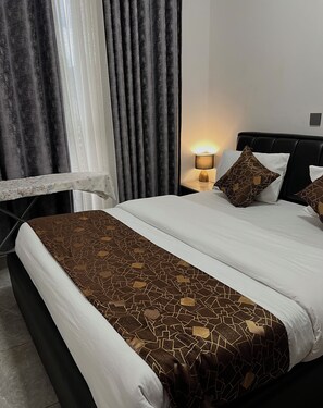 A hotel room with a bed, a nightstand, a lamp, and curtains. - CosyNook apartments (Kigali)
