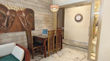 Una habitación con un panel de madera en la pared, un juego de comedor de madera, un sofá blanco, una araña y un reloj de pared.