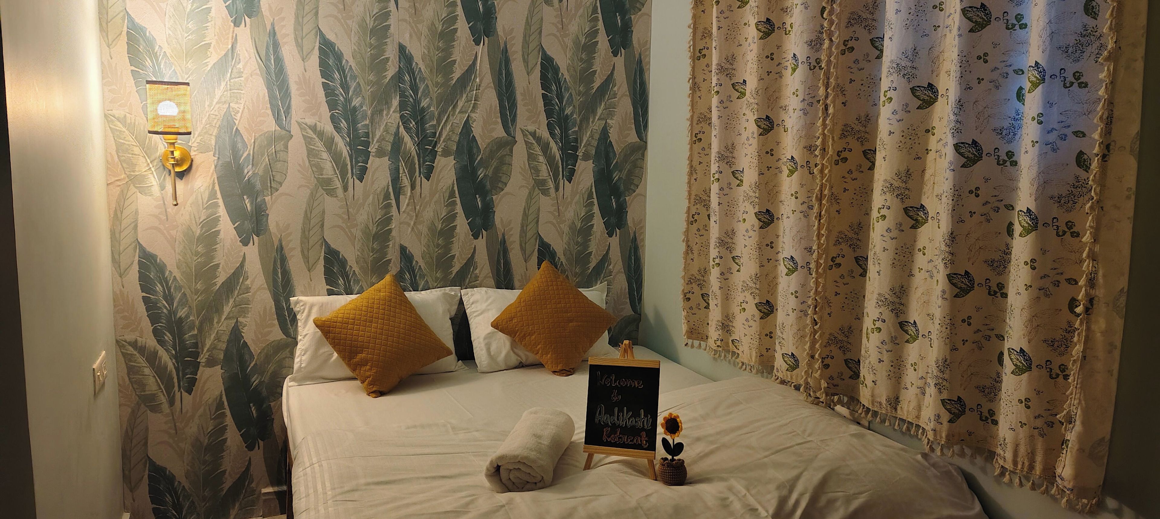 Una habitación de hotel con una cama, un cartel de bienvenida, una planta pequeña y cortinas.