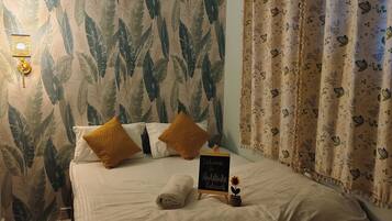 Una habitación de hotel con una cama, un cartel de bienvenida, una planta pequeña y cortinas.