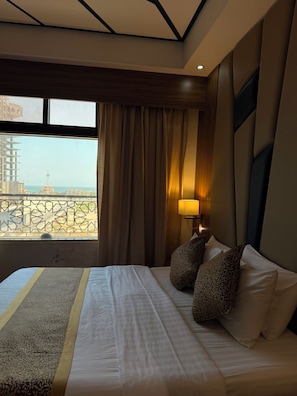 A hotel room with a large bed, a view of the cityscape, and a window with curtains. - Golden Tower Hotel (Al Khobar)