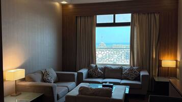 A modern hotel room with a sofa set, a coffee table, and a view of the cityscape through large windows.
