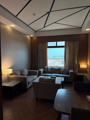A modern hotel room with a sofa set, a coffee table, and a view of the cityscape through large windows. - Golden Tower Hotel (Al Khobar)
