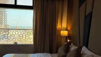 A hotel room with a bed, a window with curtains, a view of a building, and a lamp.
