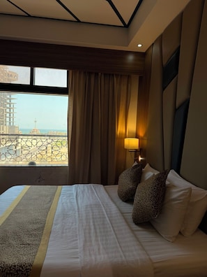 A hotel room with a bed, a window with curtains, a view of a building, and a lamp. - Golden Tower Hotel (Al Khobar)