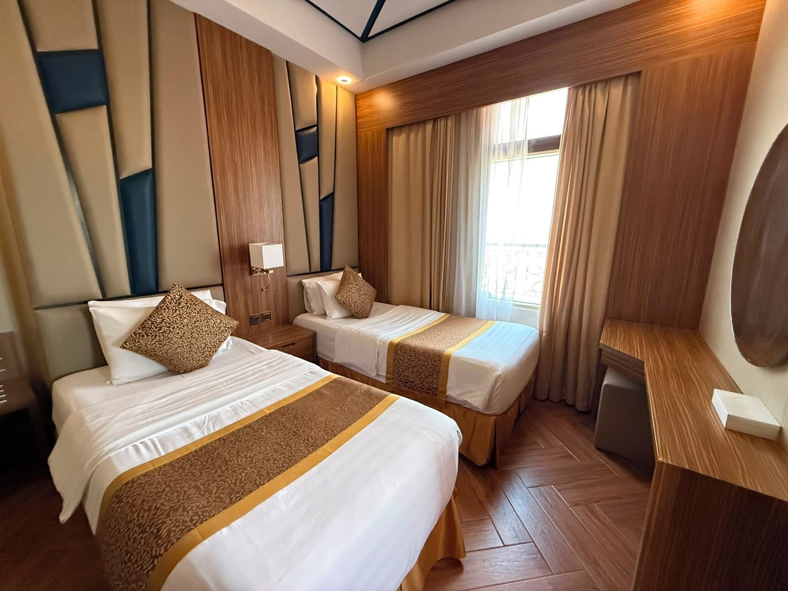 A hotel room with two beds, a desk, and a large window with curtains.