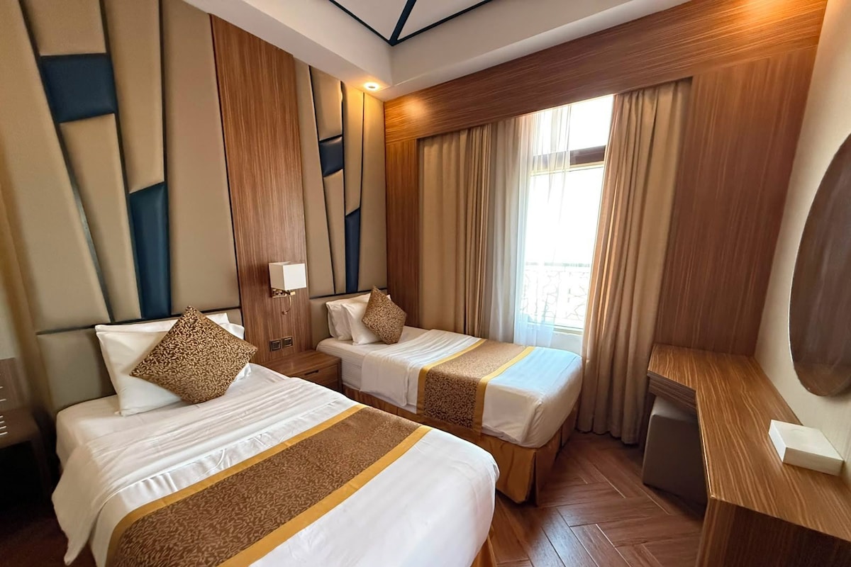 A hotel room with two beds, a desk, and a large window with curtains.