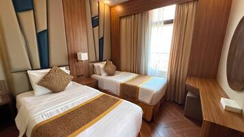 A hotel room with two beds, a desk, and a large window with curtains.