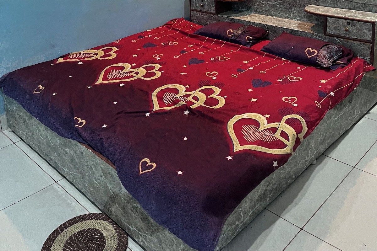 Een slaapkamer met een bed, een nachtkastje, een wand met bloemenmotieven en een plafondlamp.