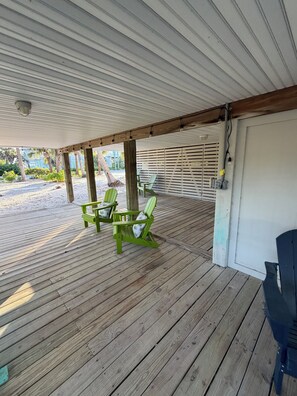 A covered outdoor area with wooden flooring, green Adirondack chairs, and a white door. - Escape the Ordinary! Unplug & Unwind on the best bridgeless Barrier Island in Fl (Placida)
