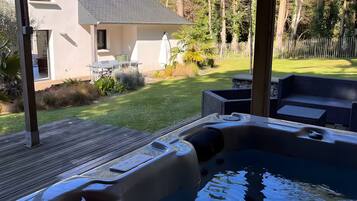 A hot tub with a wooden deck, a lawn, and a house in the background.