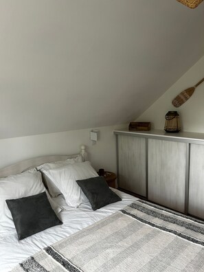 A bedroom with a bed, pillows, a bedside table, a lamp, and a wardrobe.