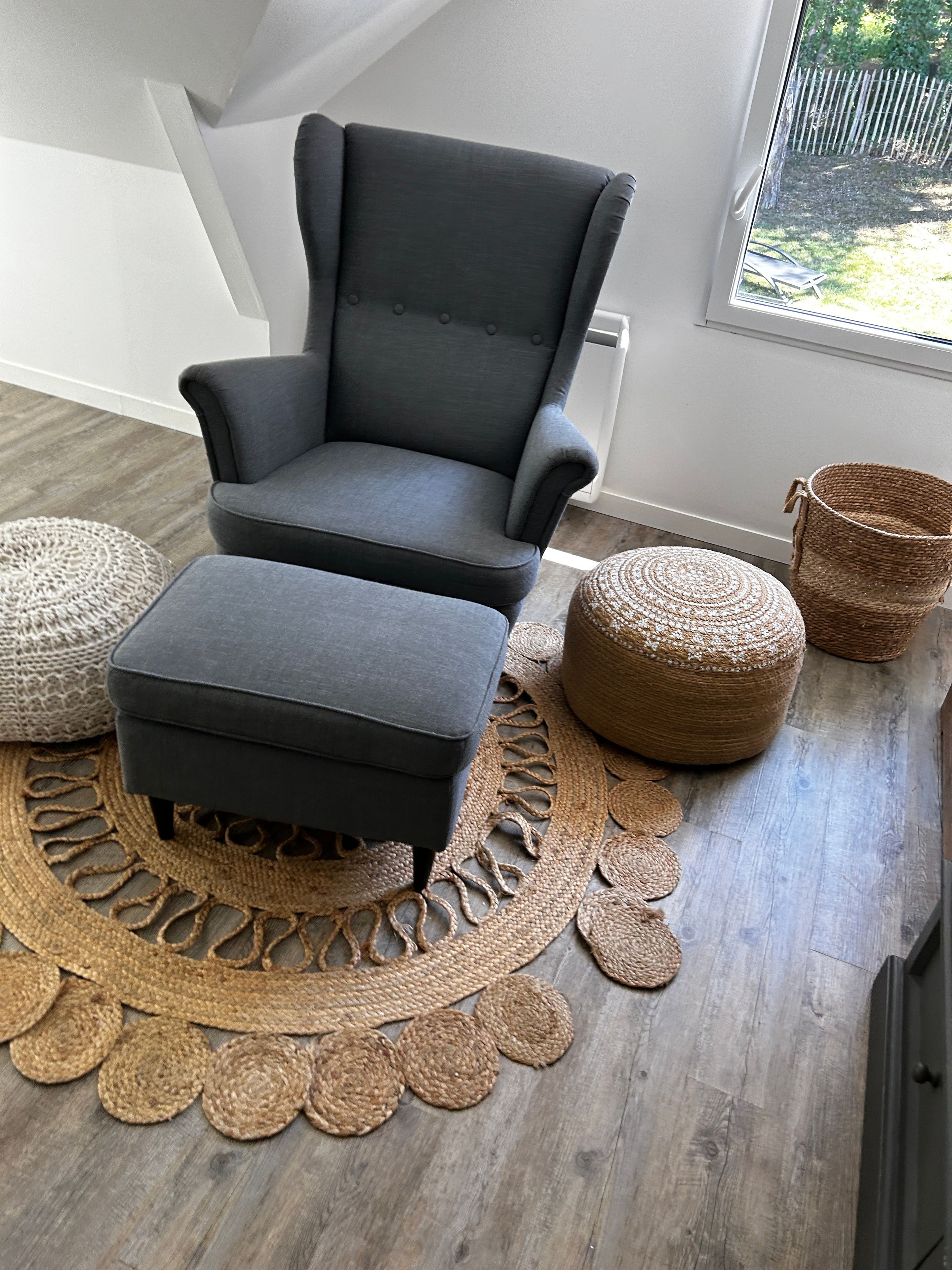 A grey armchair with a matching ottoman, a woven rug, and a wicker basket.