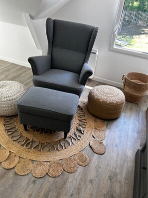 A grey armchair with a matching ottoman, a woven rug, and a wicker basket.