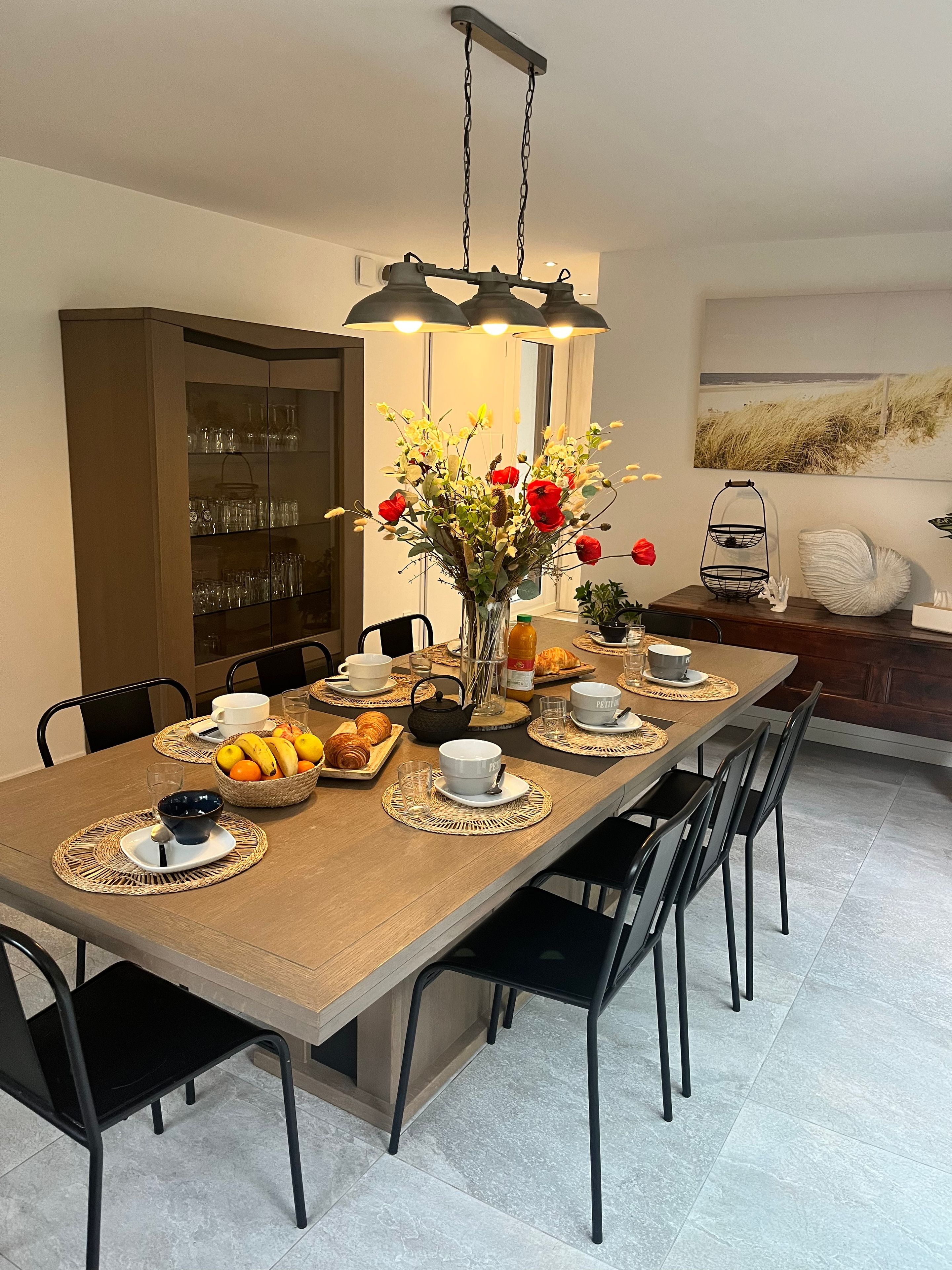 A dining area with a long table set for breakfast, including croissants, fruit, and coffee cups.