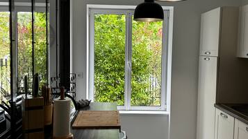 A modern kitchen with a large window, a dining table, and a hanging light fixture.