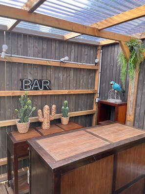 Eine Holztresorecke mit einem 'BAR'-Schild, Kakteendekoration und einem Papagei auf einem Sitzstab.