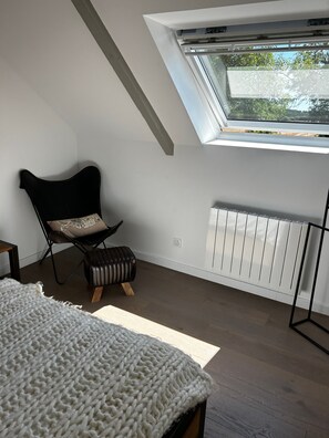 Ein Zimmer mit schrägen Wänden, einem schwarzen Stuhl mit Sitzkissen, einem weißen Heizkörper und einem Holzboden.