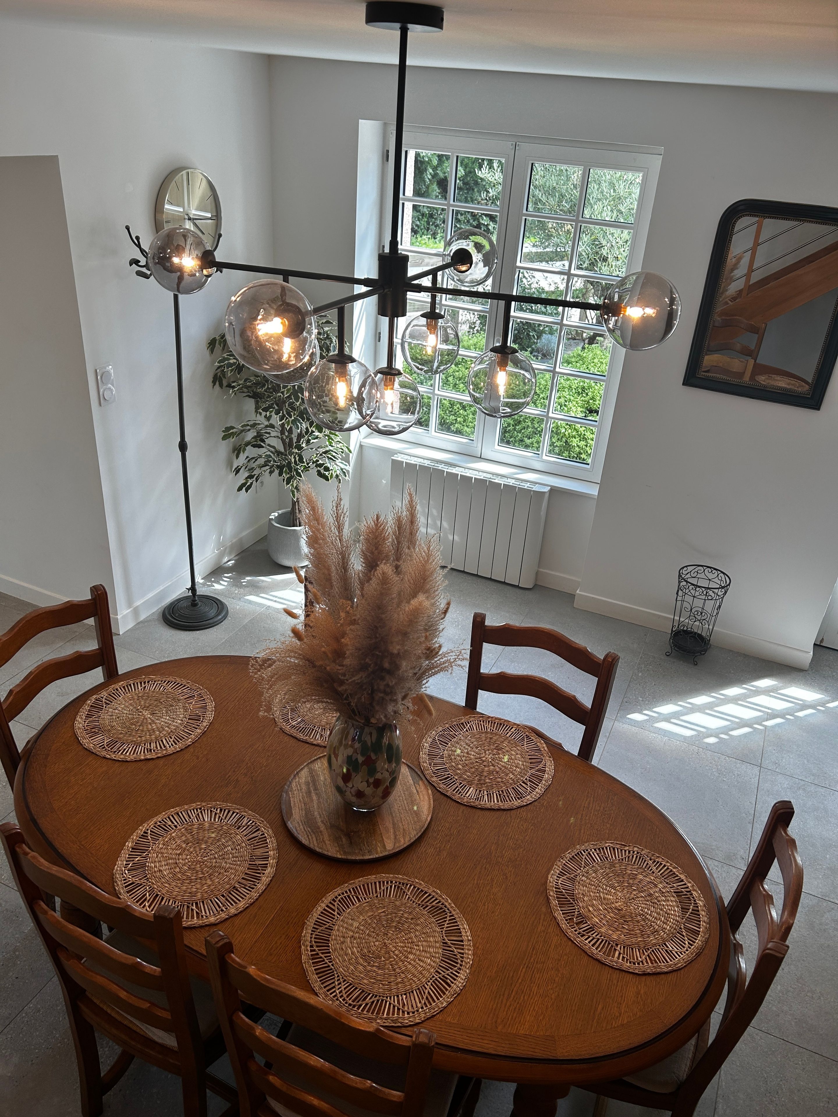 Een eetgedeelte met een ronde houten tafel, geweven placematen en een centraal vaasje met gedroogde planten.