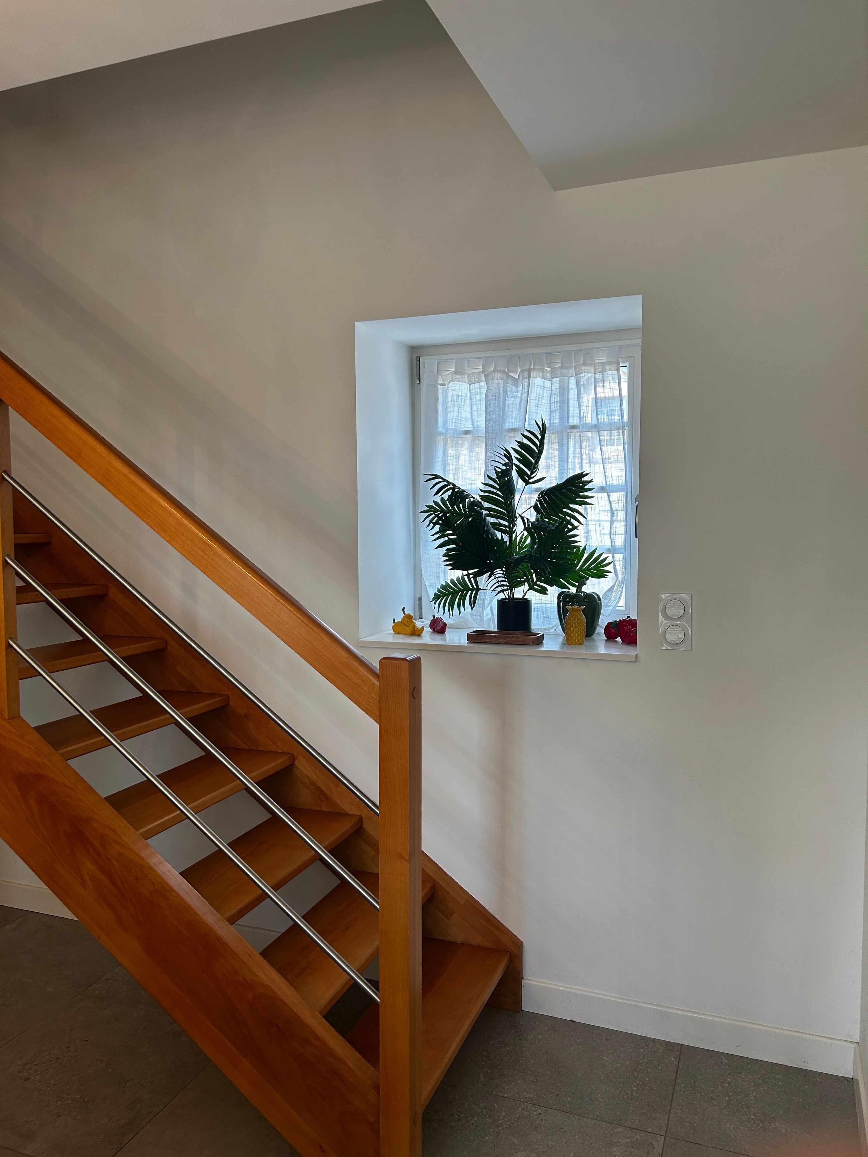 Een houten trap met een witte muur en een klein raam met een plant.