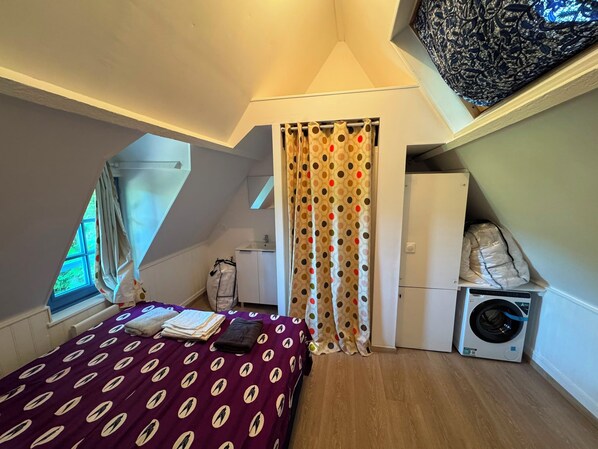 Une petite pièce, de taille modeste, comprenant un lit, un lave-linge et une fenêtre.