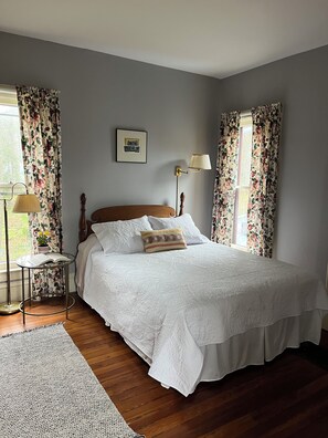 Un lit bien fait, avec une couette blanche, une table de chevet avec une lampe et des rideaux à motifs floraux.