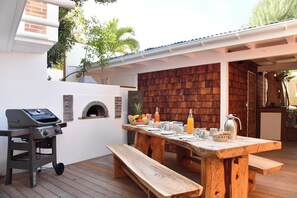 Uma área externa para refeições com mesa e bancos de madeira, churrasqueira e forno de tijolos.