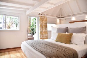 Ein Schlafzimmer mit einem großen Bett, einem Fenster mit Vorhängen und Blick auf Grünfläche.