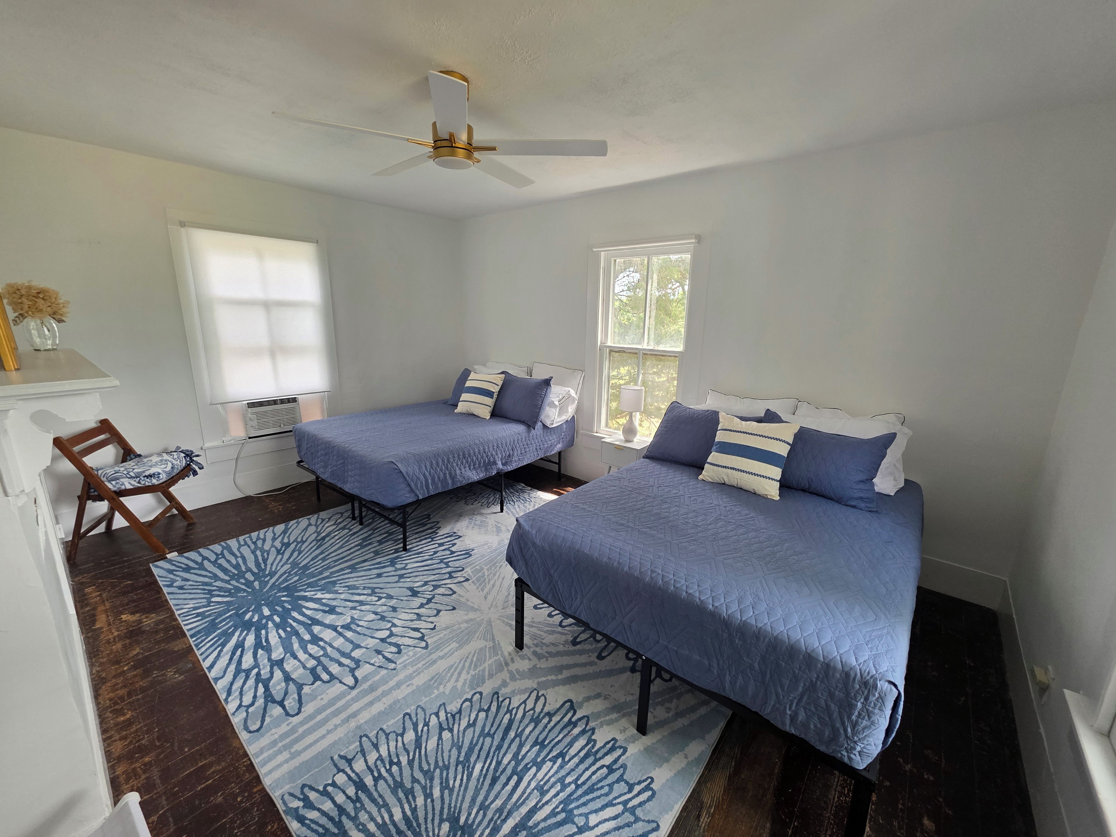 A bedroom with two beds, a ceiling fan, a window, and a wooden chair.