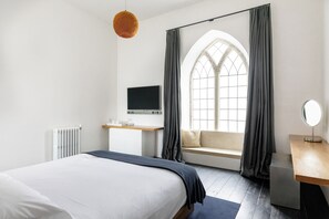 A modern bedroom with a bed, a desk with a computer, a window with curtains, and a hanging light fixture. - At The Chapel (Bruton)