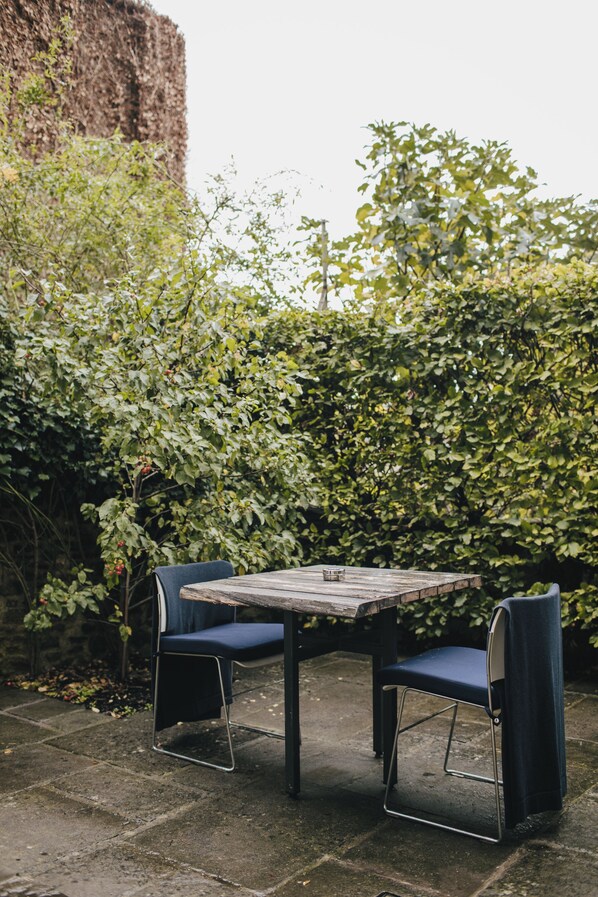 An outdoor seating area with a table and two chairs, surrounded by dense foliage. - At The Chapel (Bruton)