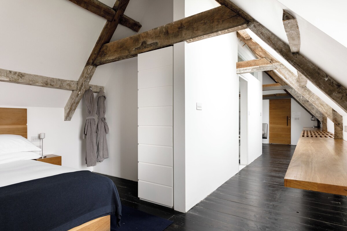 A bedroom with a wooden ceiling, a bed, a nightstand, and a wall-mounted towel rack.