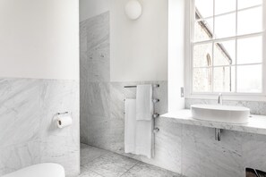 A modern bathroom with a marble floor, a white sink, and a window with a view of a building. - At The Chapel (Bruton)
