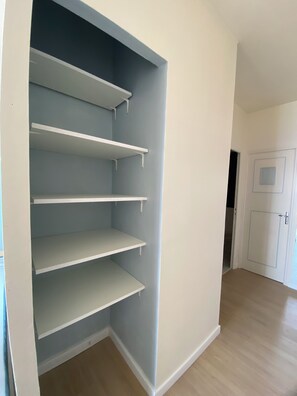 Ein Zimmer mit integriertem Kleiderschrank, der mehrere Regale und eine Tür mit einem quadratischen Fenster bietet.