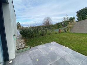 Une terrasse carrelée de dalles grises, une pelouse et une haie.